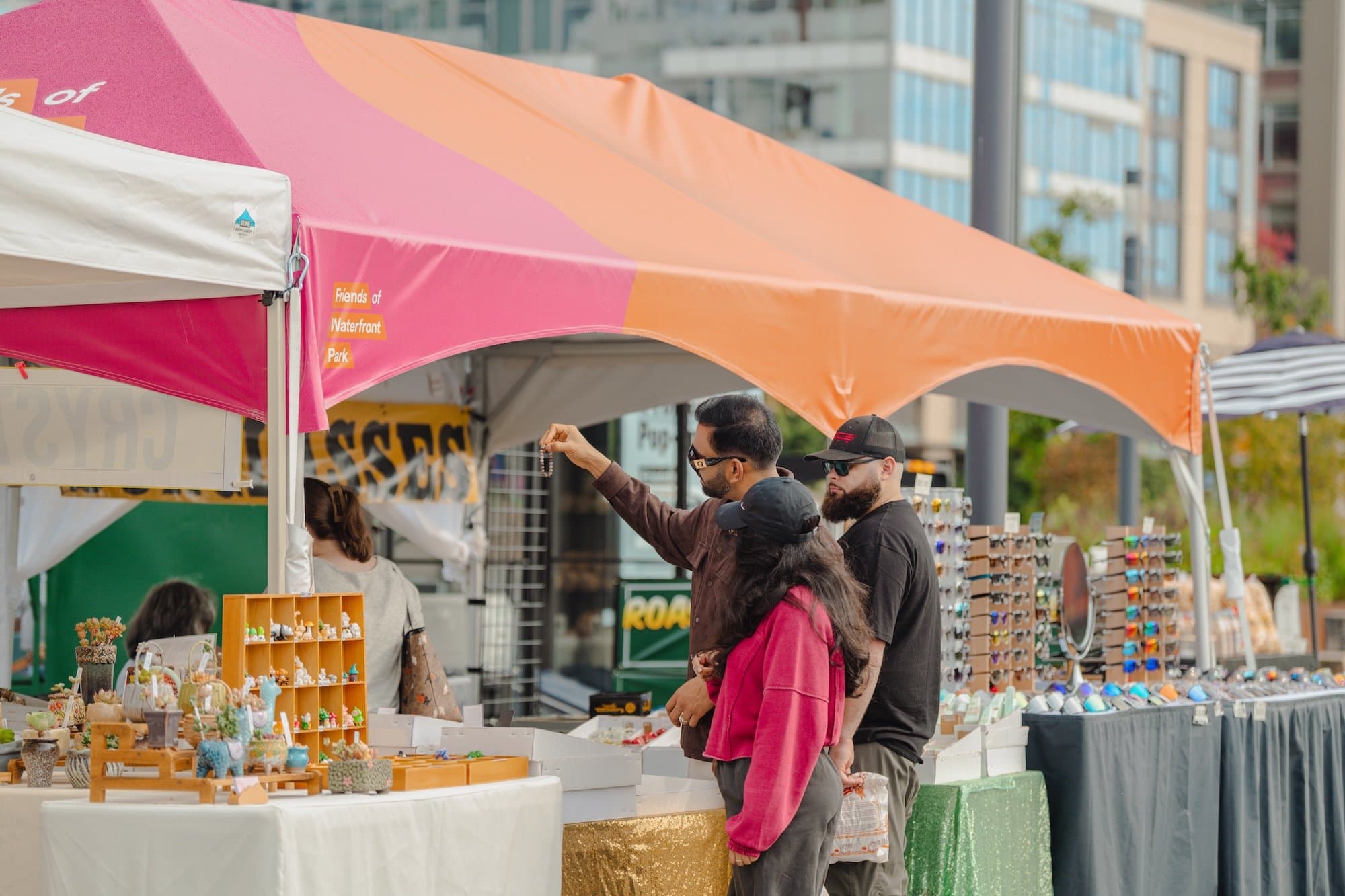 Three people peruse a pop-up vendor with an assortment of items at the Waterfront Park Market that happened throughout summer 2025.