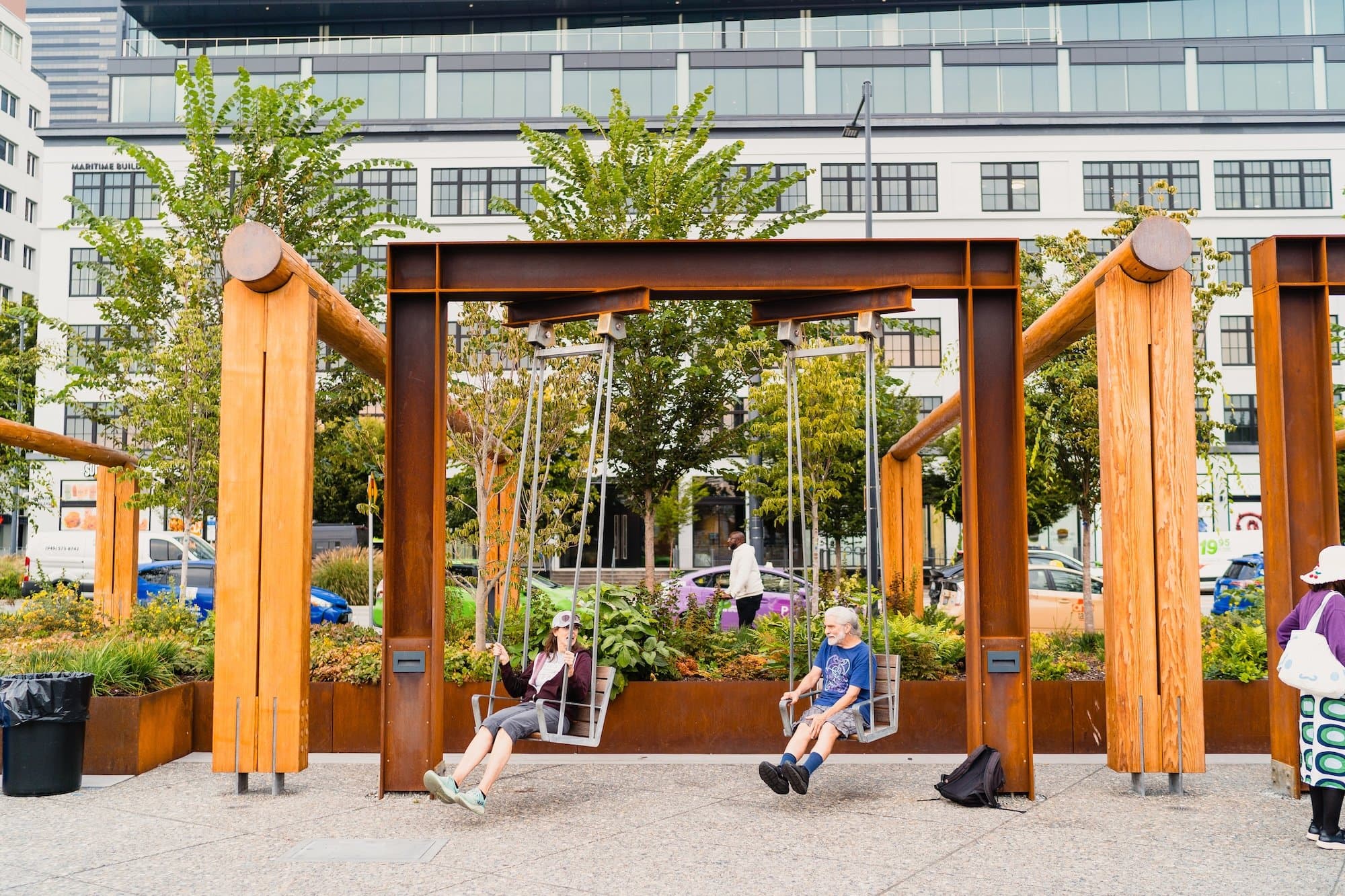 Two people enjoy the large swings on the Waterfront Park Promenade.