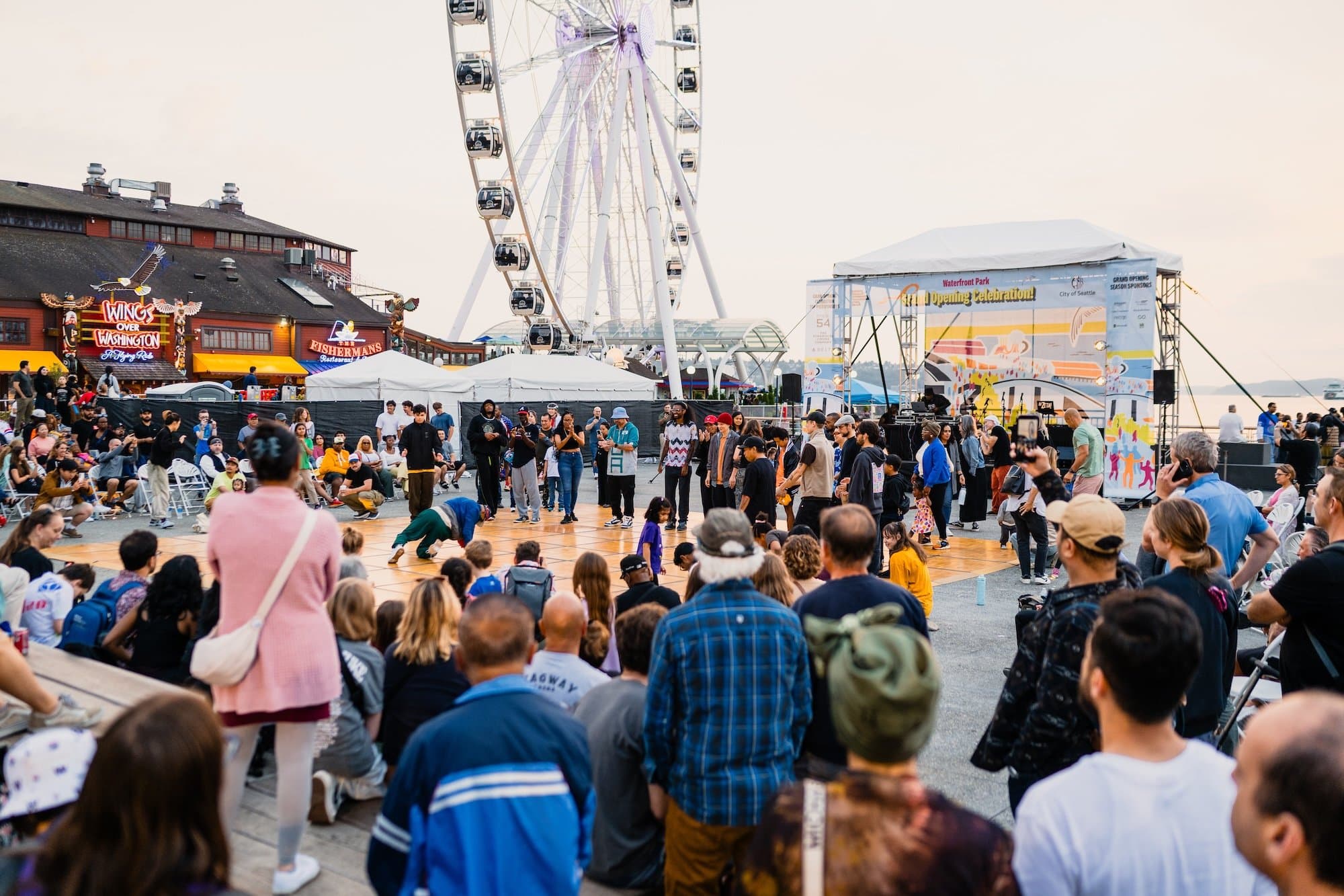 Large crowds gather on Pier 58 watching performers on a dance floor, with the Great Wheel and Waterfront Park's Grand Opening stage in the background.
